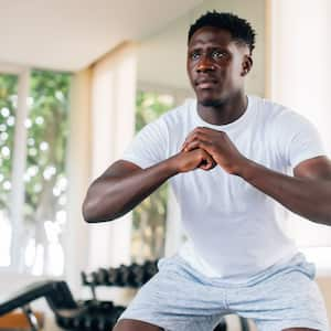 An African American man in a white shirt doing squats in his home gym